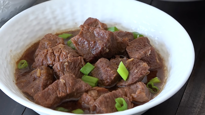 A White Bowl Filled with Tender Beef Pares in A Rich, Savory Sauce, Garnished with Chopped Green Onions