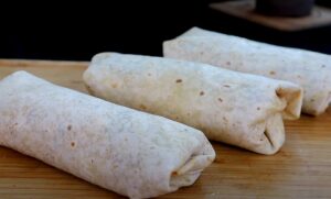 Freshly made burritos, resting on a wooden board