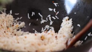 Cooked Rice Is Being Stir-Fried with Crispy Garlic and Seasonings in A Wok Using a Wooden Spatula