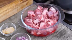 A Glass Bowl Filled with Raw Cubed Beef, Surrounded by Small Bowls of Sliced Ginger, Chopped Onions